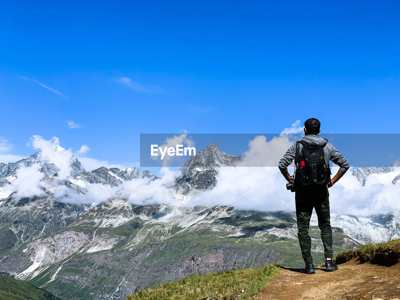 Rear view of man looking at mountains against blue sky