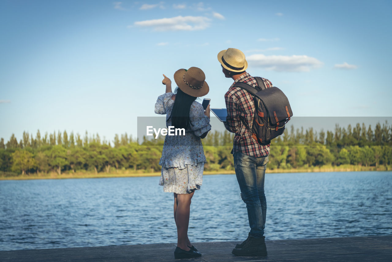 REAR VIEW OF FRIENDS STANDING ON LAKE AGAINST SKY