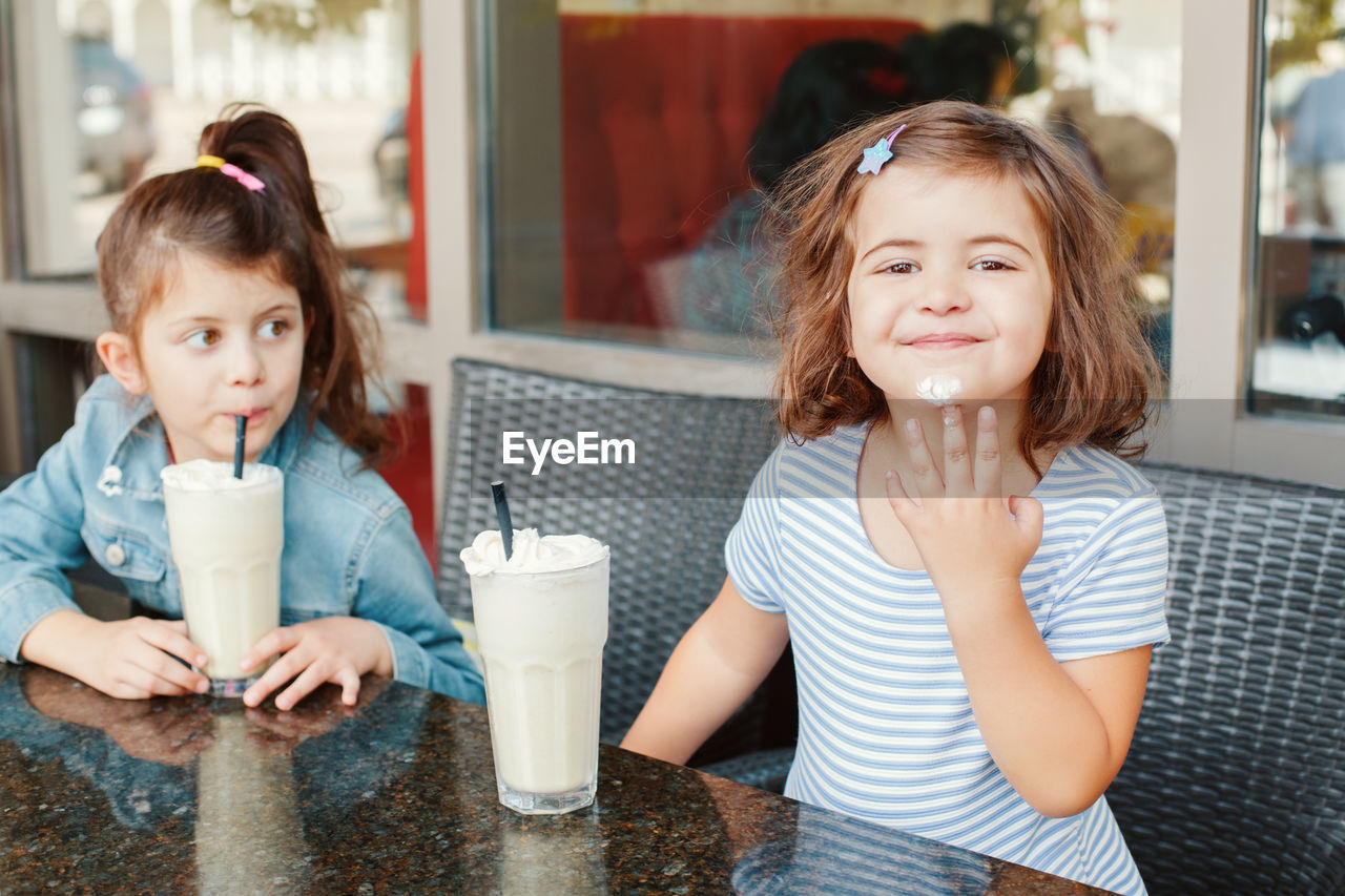 Happy siblings enjoying milk shake at table in coffee shop