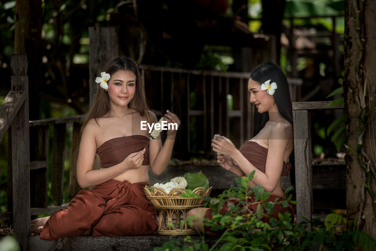 Portrait of young women in traditional clothing holding flowers while sitting outdoors