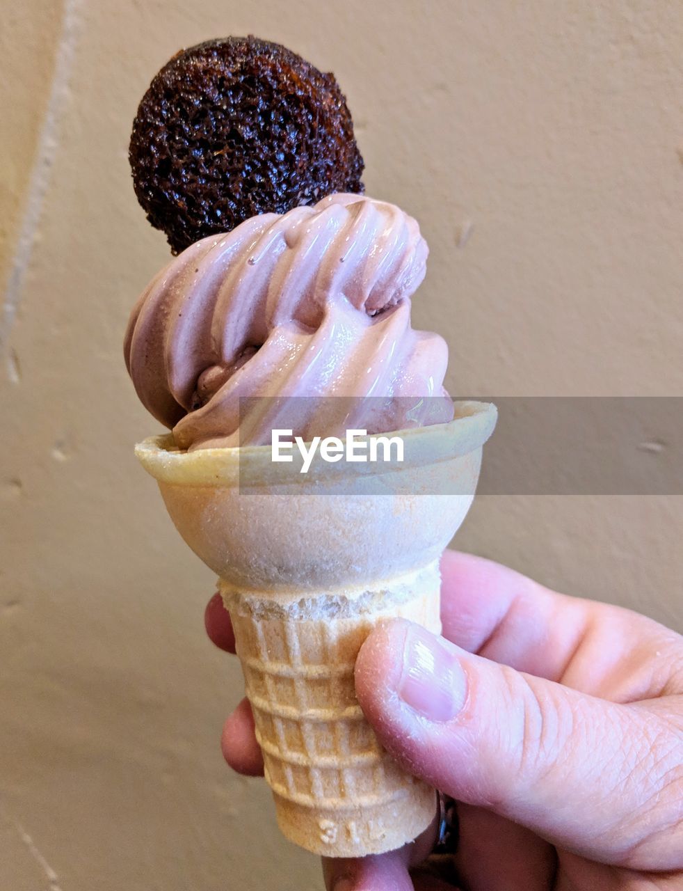 CLOSE-UP OF HAND HOLDING ICE CREAM CONE AGAINST BLURRED BACKGROUND