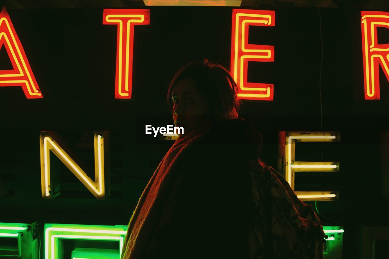 Portrait of woman standing by illuminated text at night