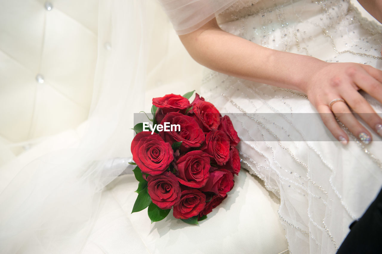 Midsection of bride with red roses bouquet