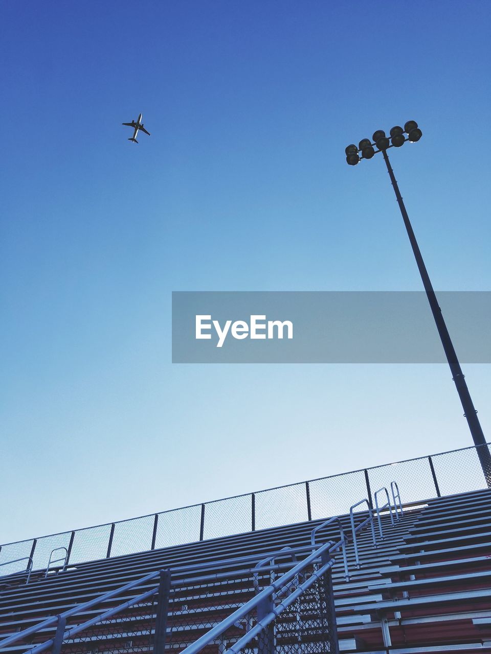 Low angle view of stadium against airplane flying in clear blue sky