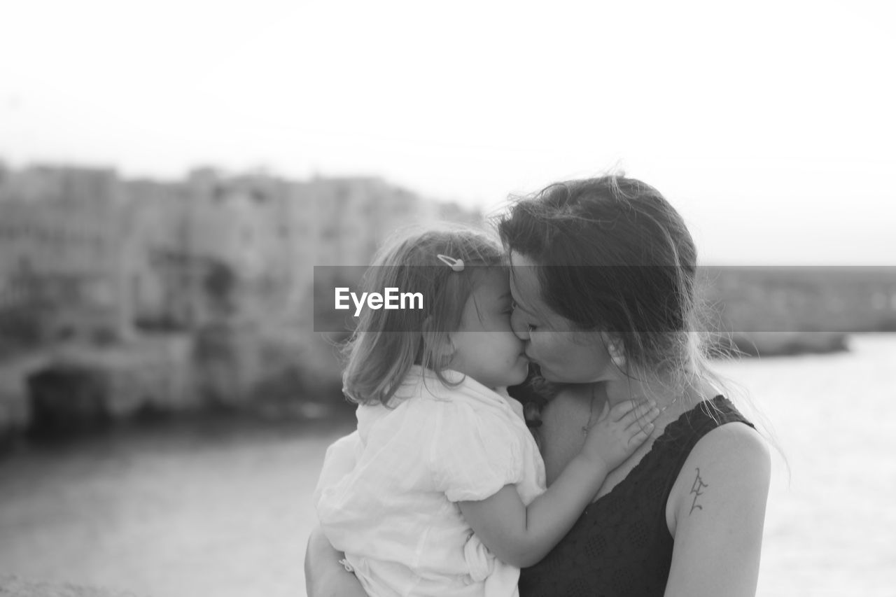 Close-up of mother kissing by daughter by river against sky