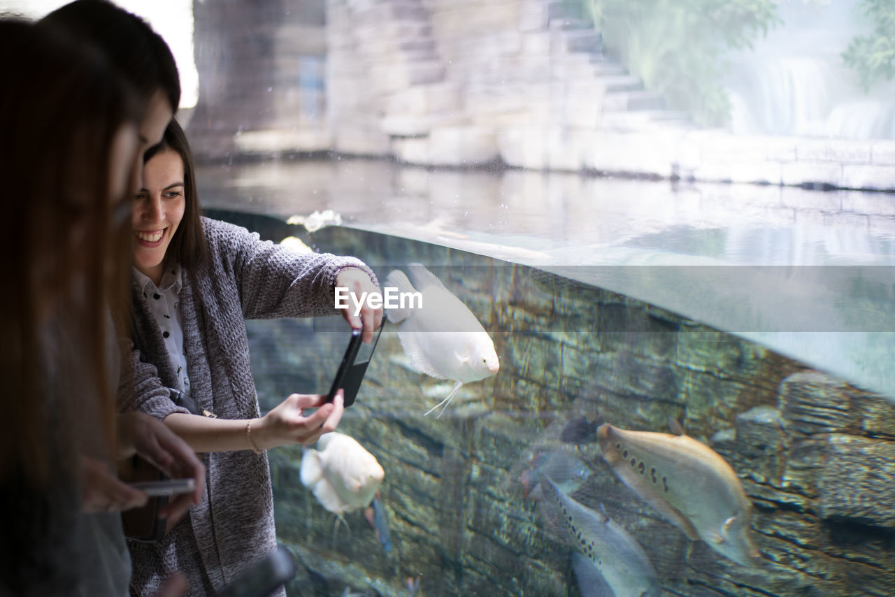 Smiling young woman photographing fish in aquarium