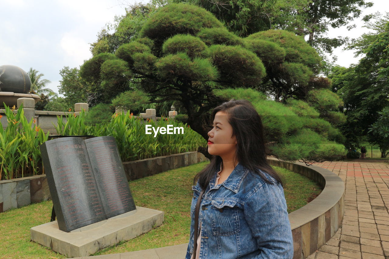 Side view of smiling woman standing against trees