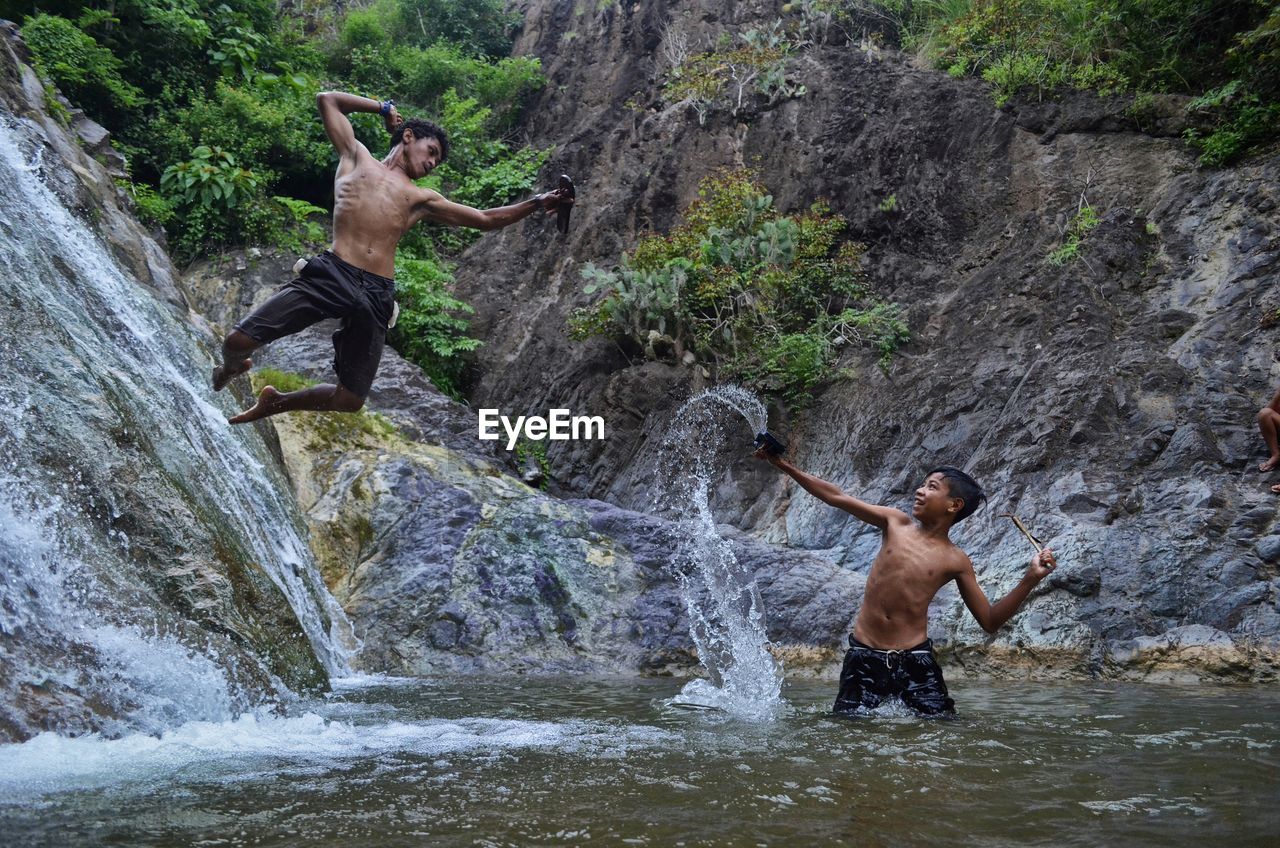 Full length of shirtless man standing on rock against waterfall