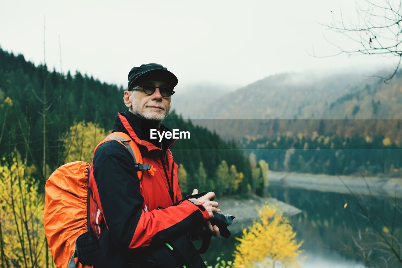 Portrait of man standing by lake against mountains