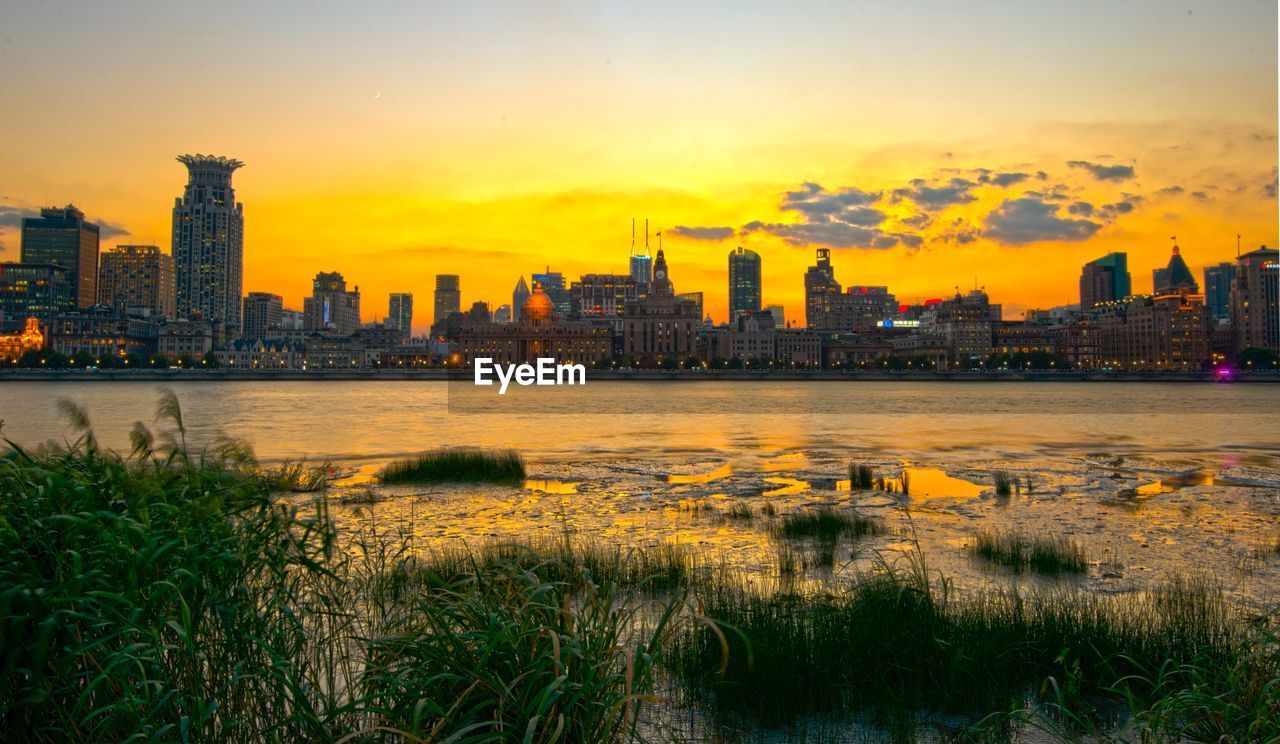 Scenic view of river by buildings against sky during sunset