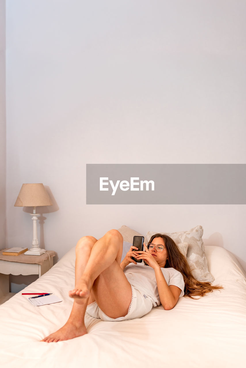 Young woman using phone while lying on bed