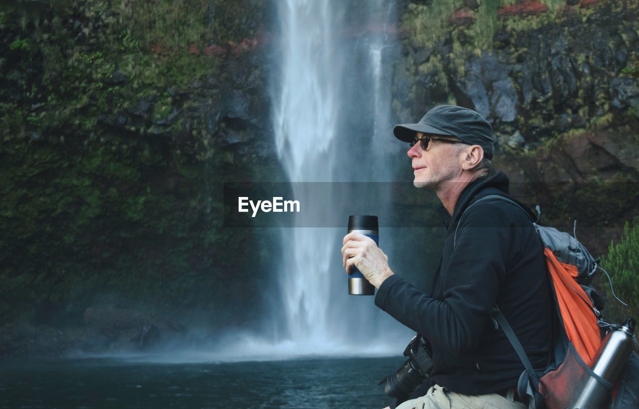 Man holding water bottle against waterfall