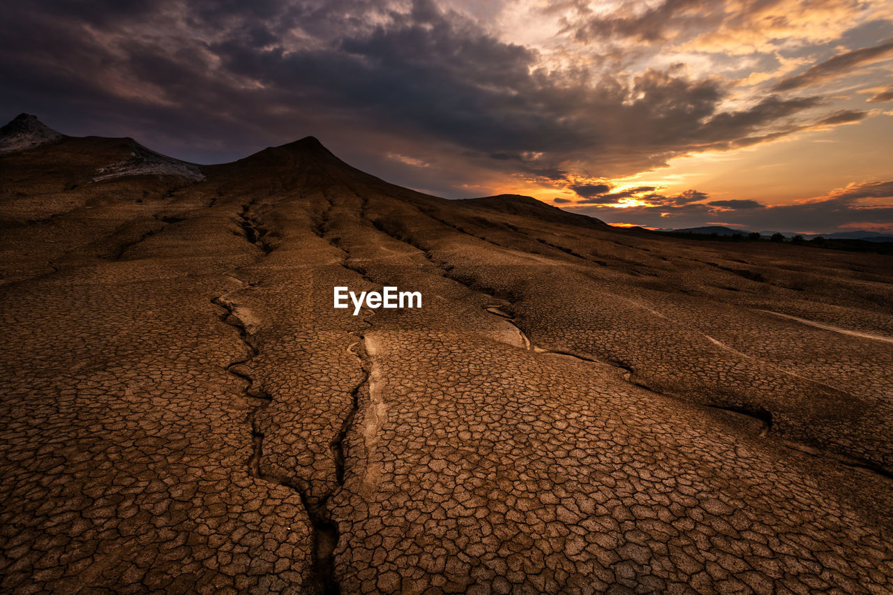 Scenic view of cracked landscape against cloudy sky during sunset