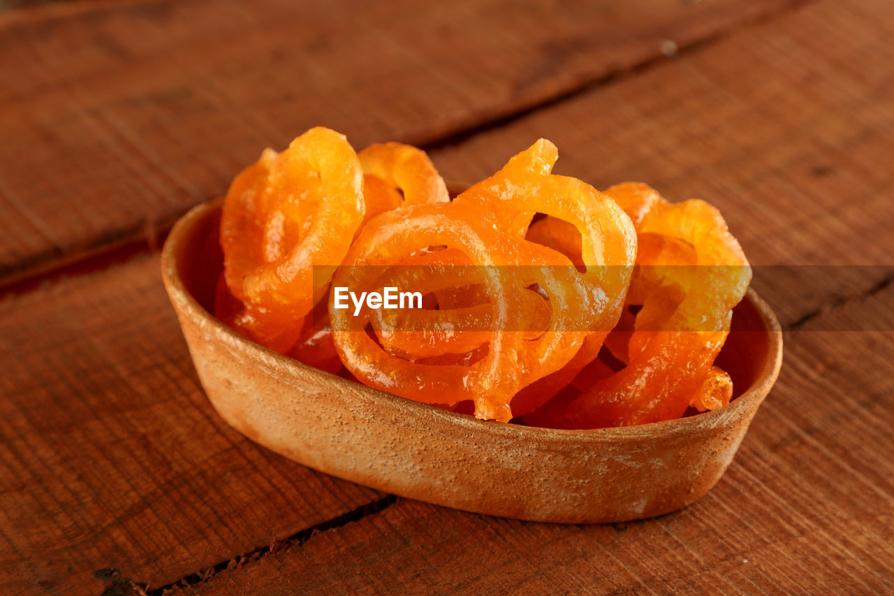 Indian sweet jalebi in a handmade pottery bowl on wooden background