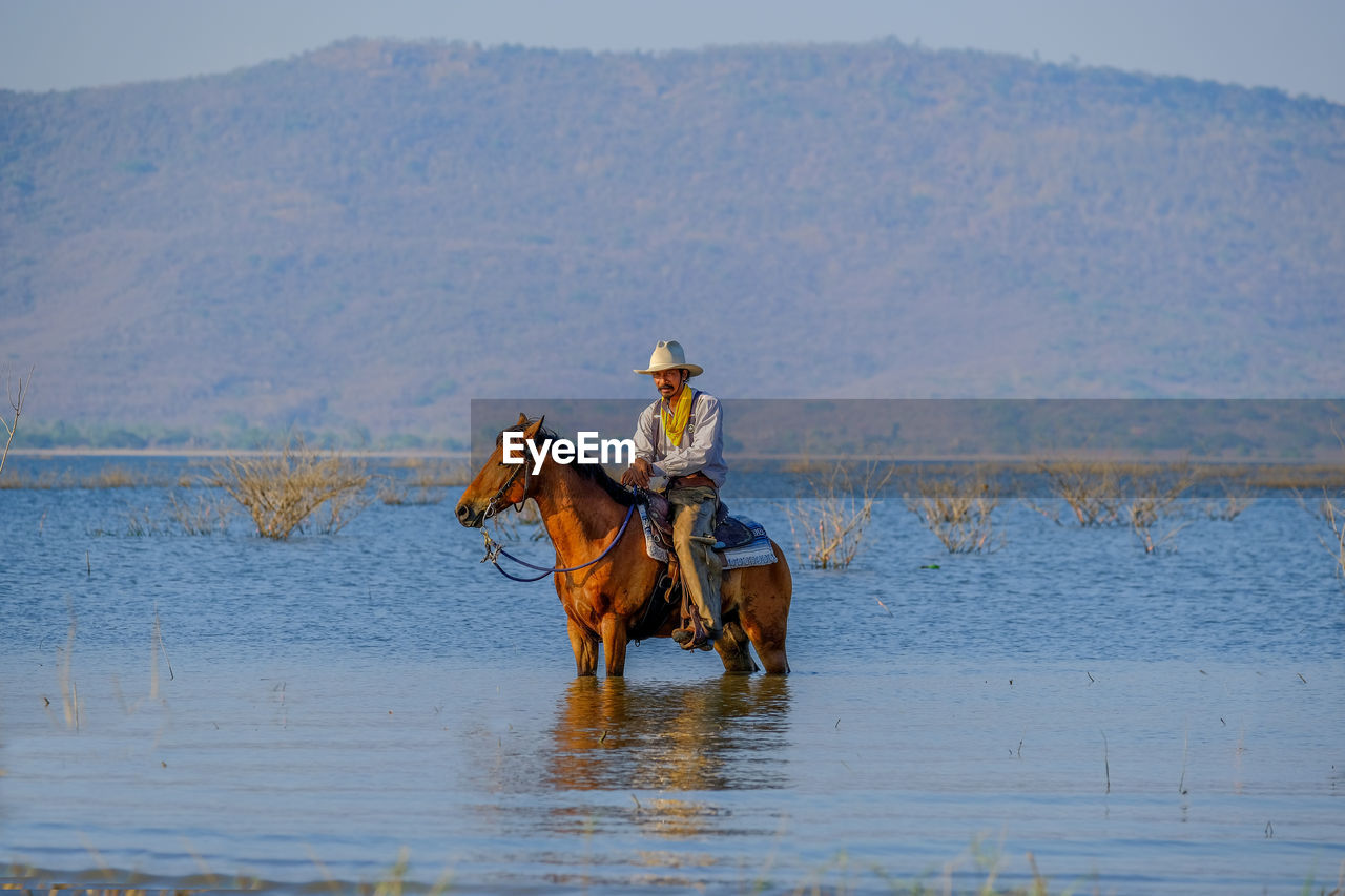Mature man riding horse in lake against mountain