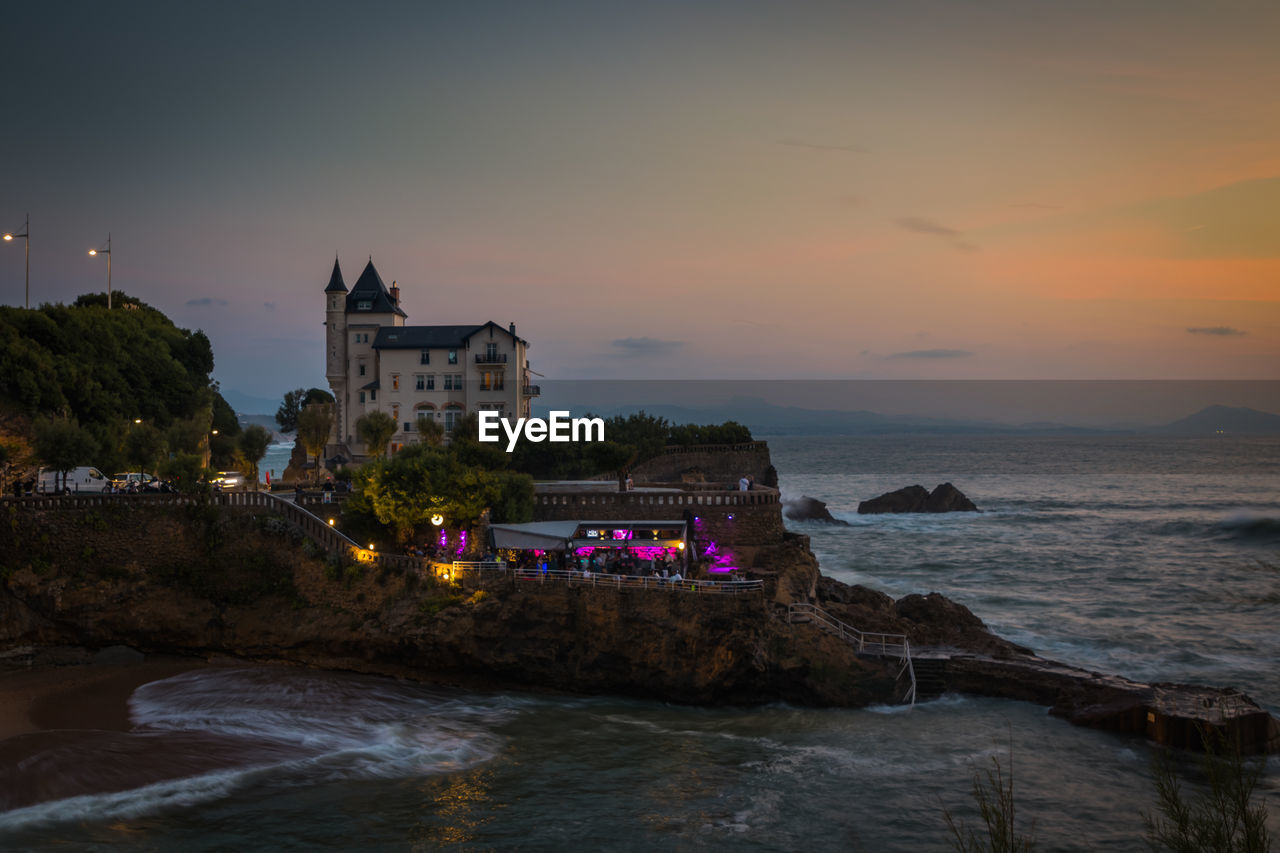 Buildings by sea against sky at sunset