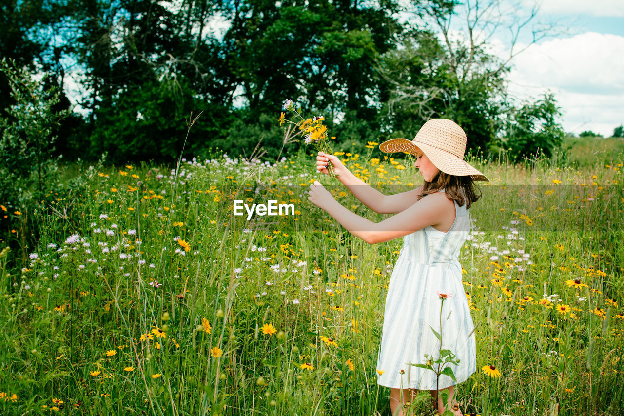 Teen girl holding a flower standing in wildflower field