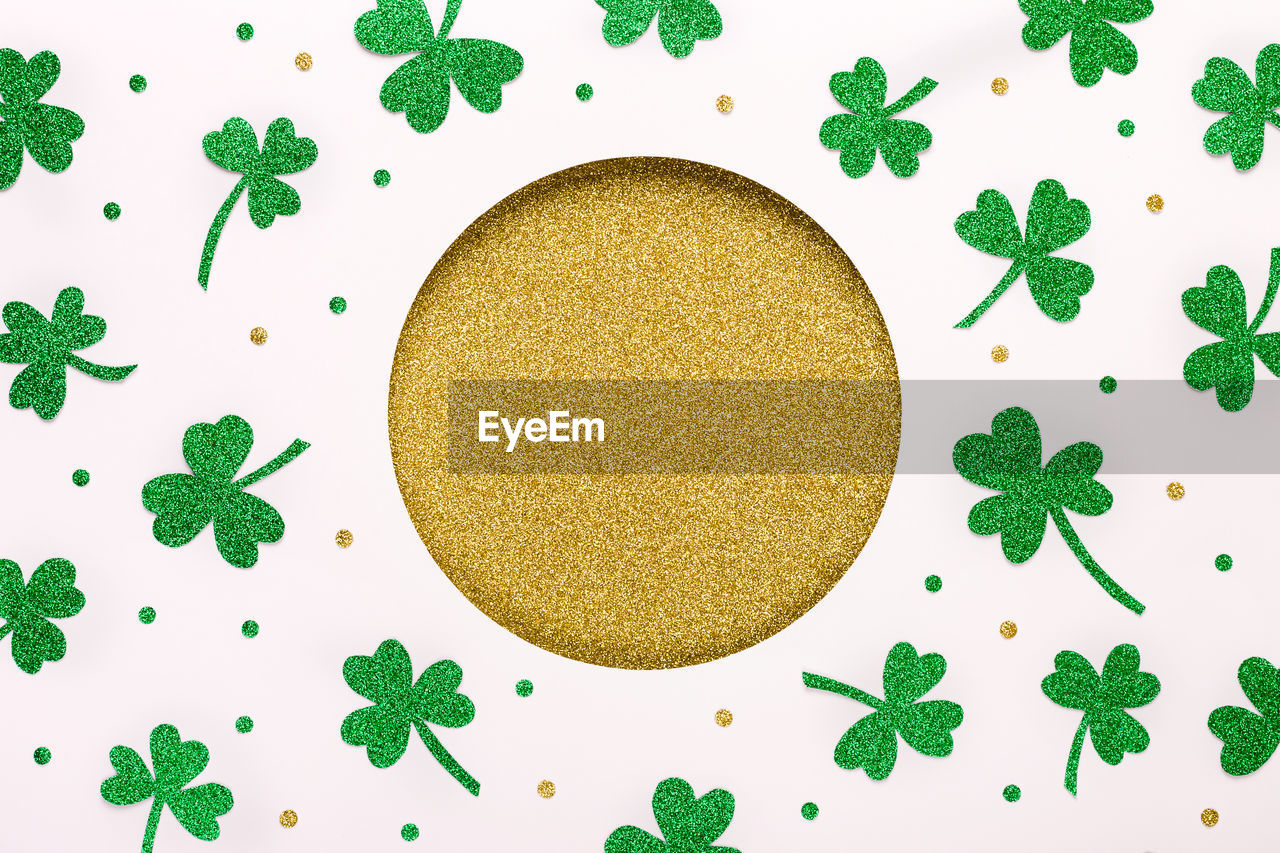 St. patricks day background. round frame of shiny shamrocks and confetti on rough wooden background.