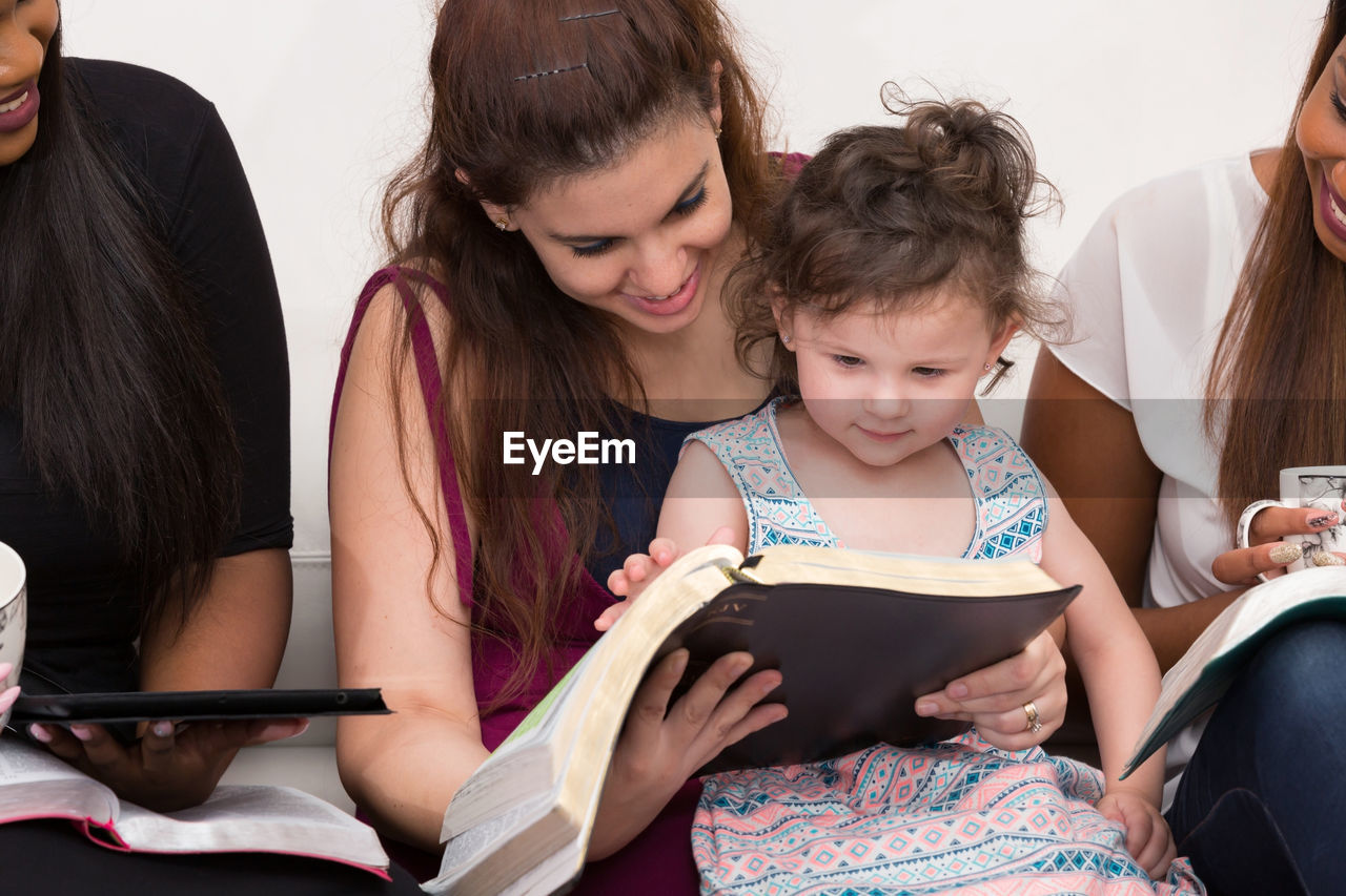 Happy young woman sitting reading book with daughter at home