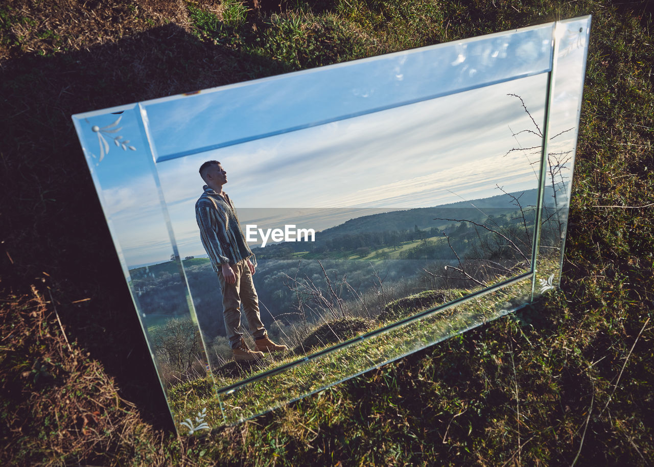 Young man and landscape reflecting on mirror 