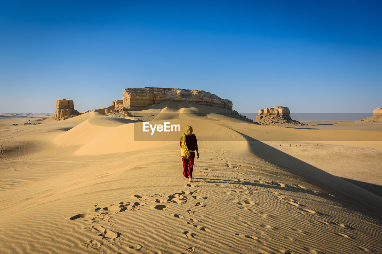 Woman walking on sand dune in desert against clear sky