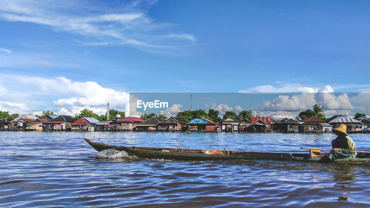 Man sitting on boat in river against sky