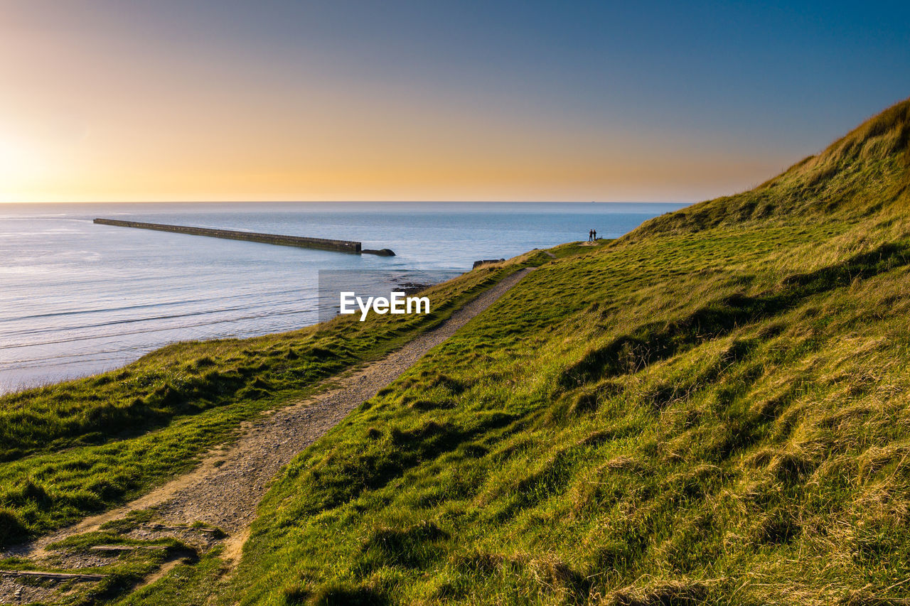 Couple enjoying elevated view of a ancient military pier just prior sunset at pointe de la crèche