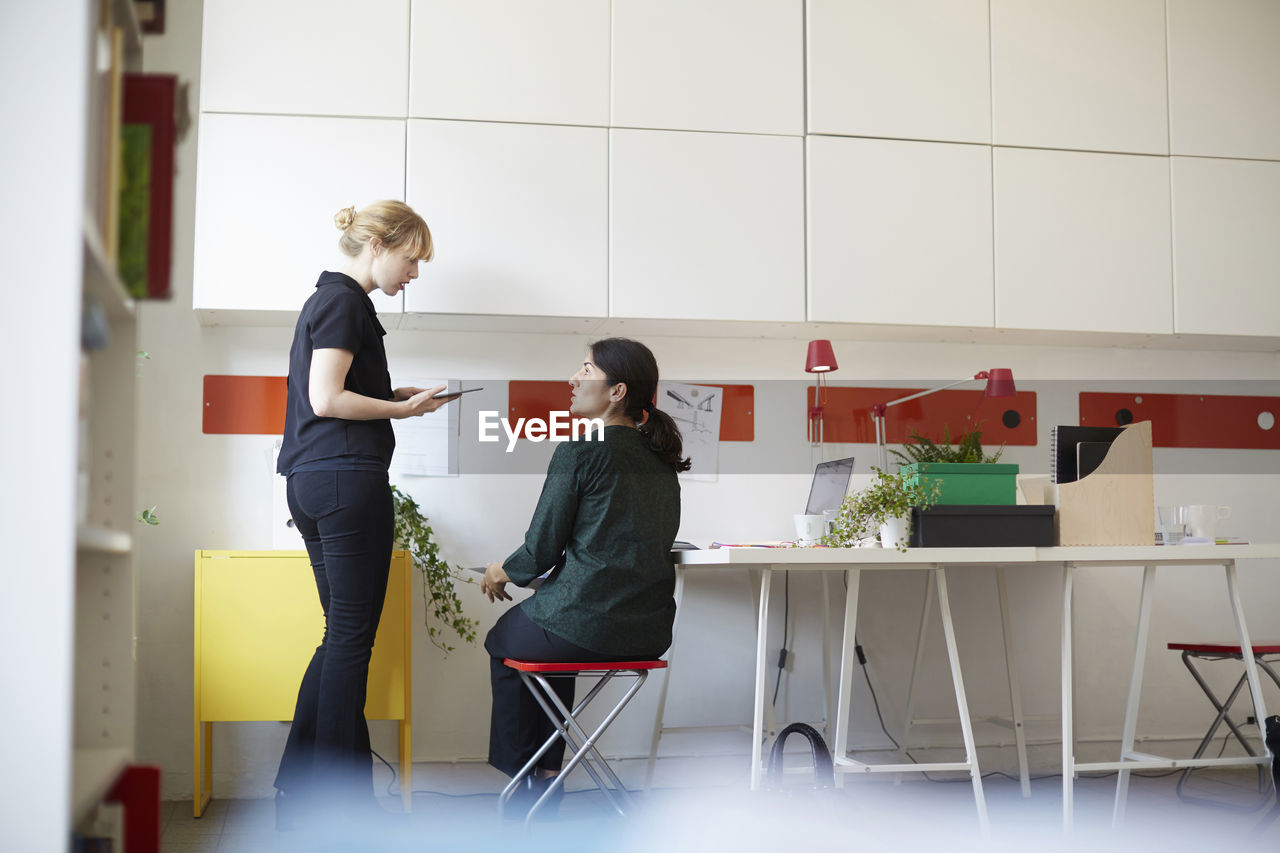 Mid adult businesswoman talking with female colleague in office