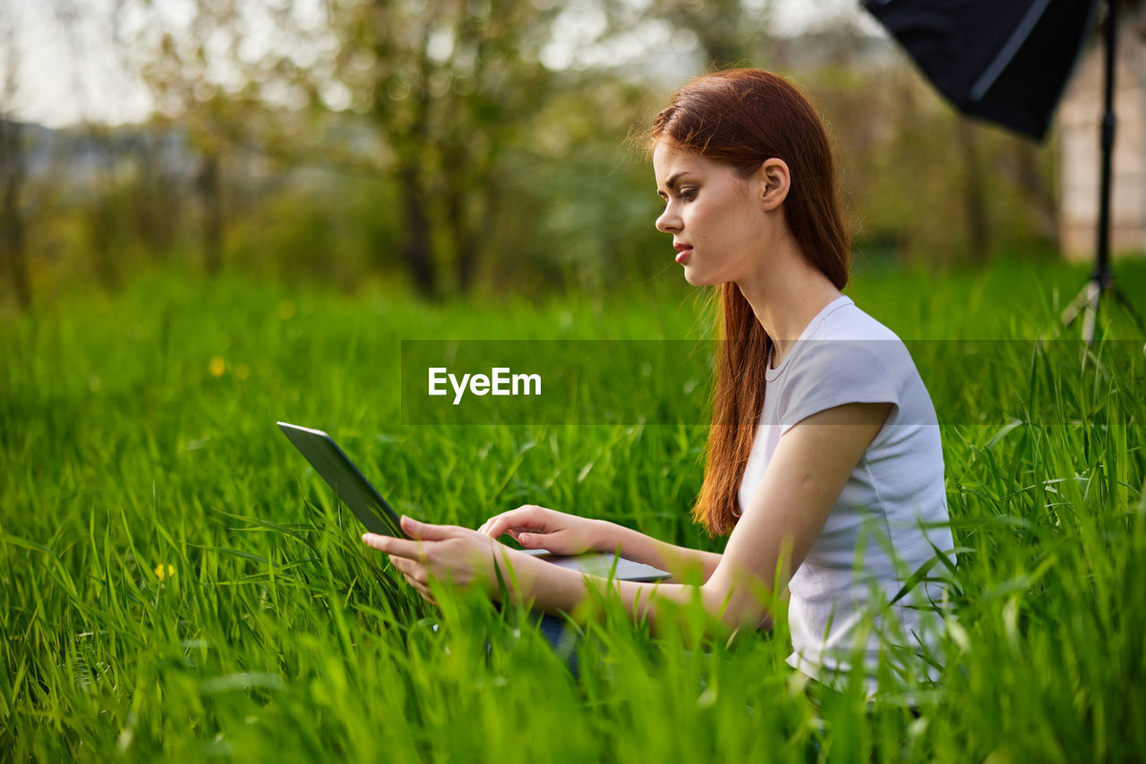 side view of young woman using mobile phone while sitting on field