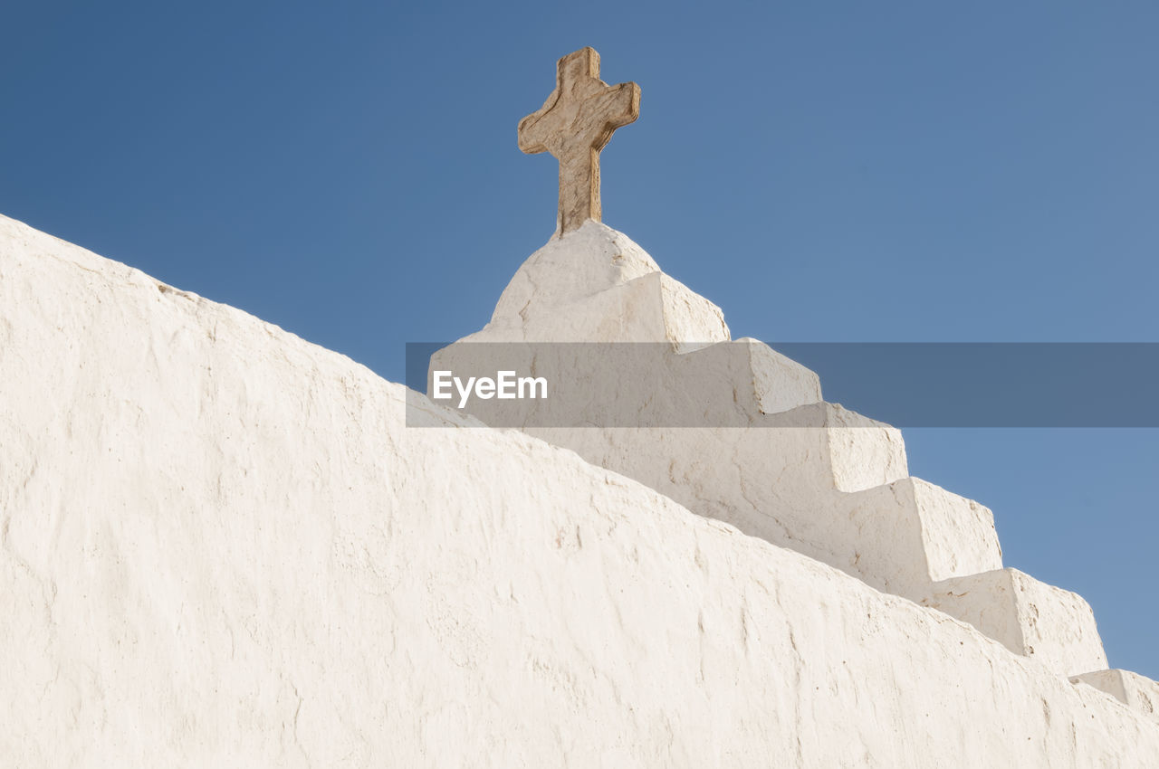 Close-up of a white roof exterior of a church with a stone cross, greece, cyclades islands, mykonos.