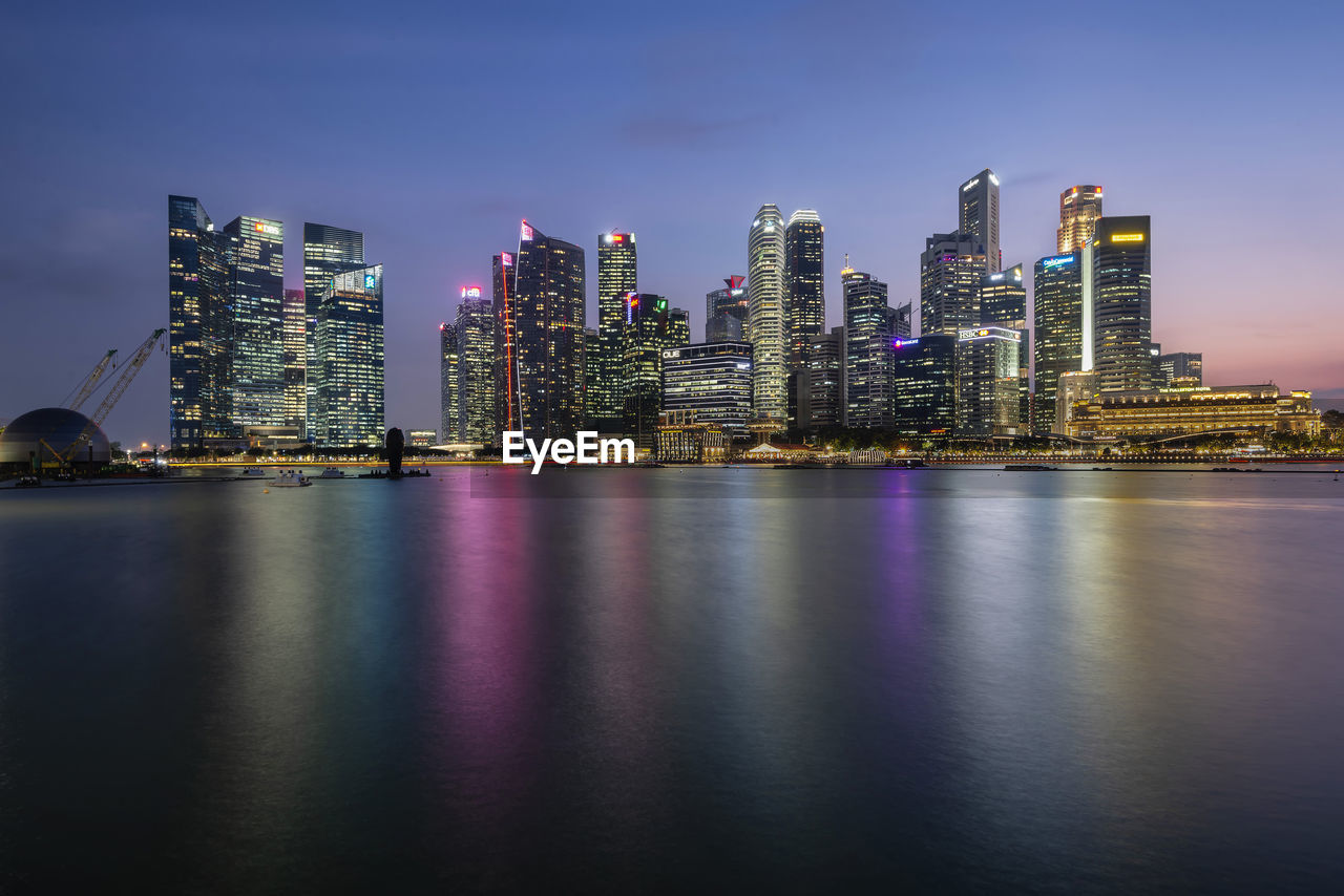 Illuminated modern buildings in city against sky at night