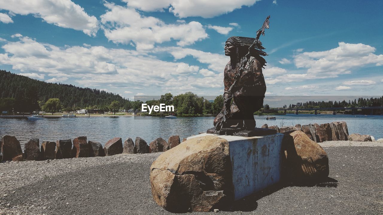 STATUE BY RIVER AGAINST SKY