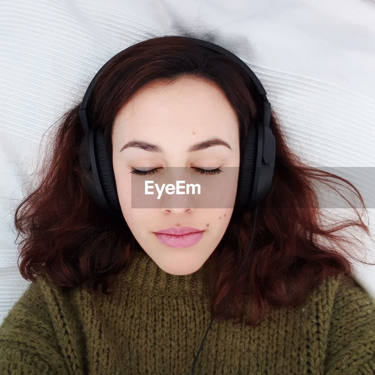 Directly above shot of young woman listening to music through headphones while lying on bed