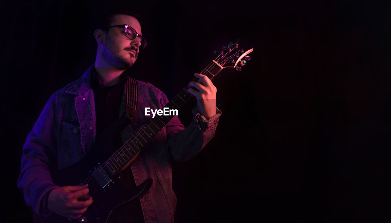 Young adult plays electric guitar under colored lights