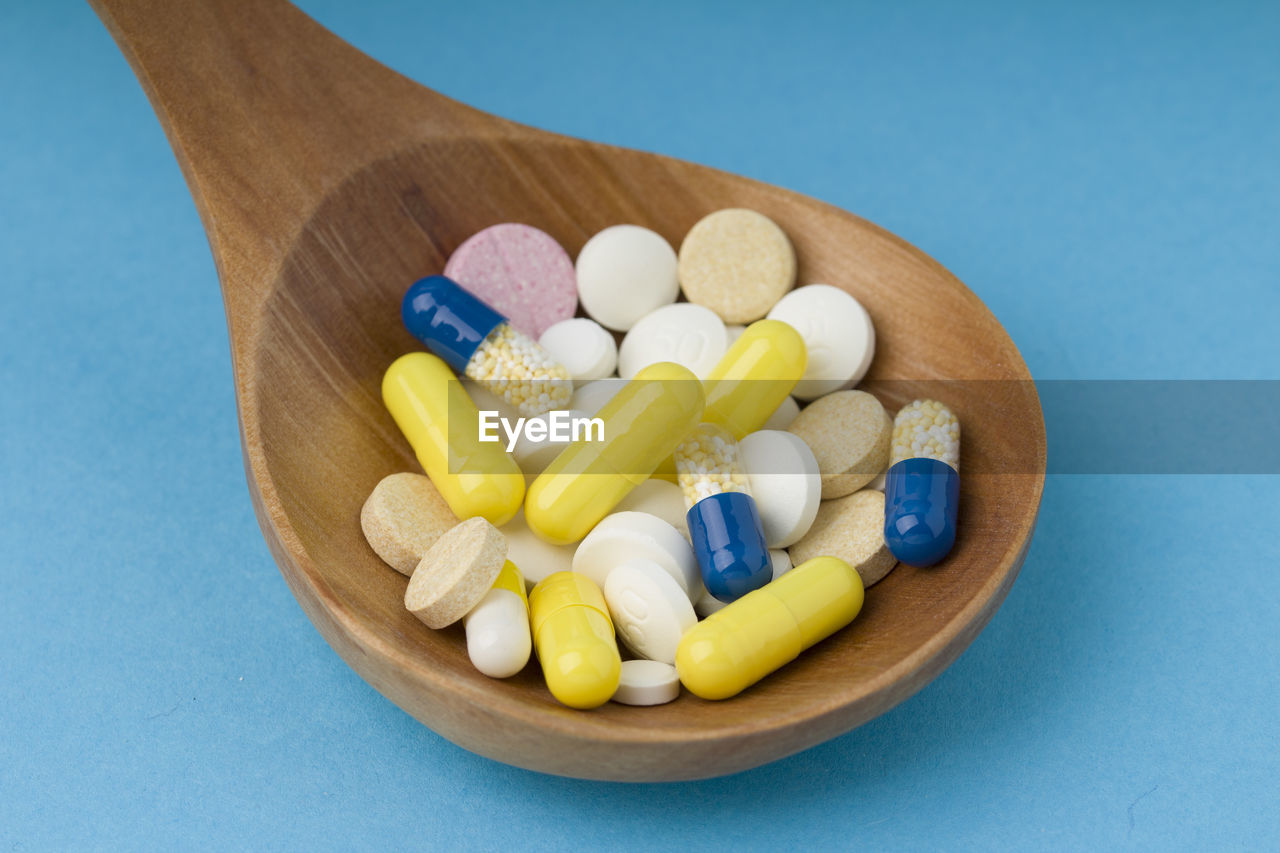 High angle view of medicines in wooden spoon on blue background