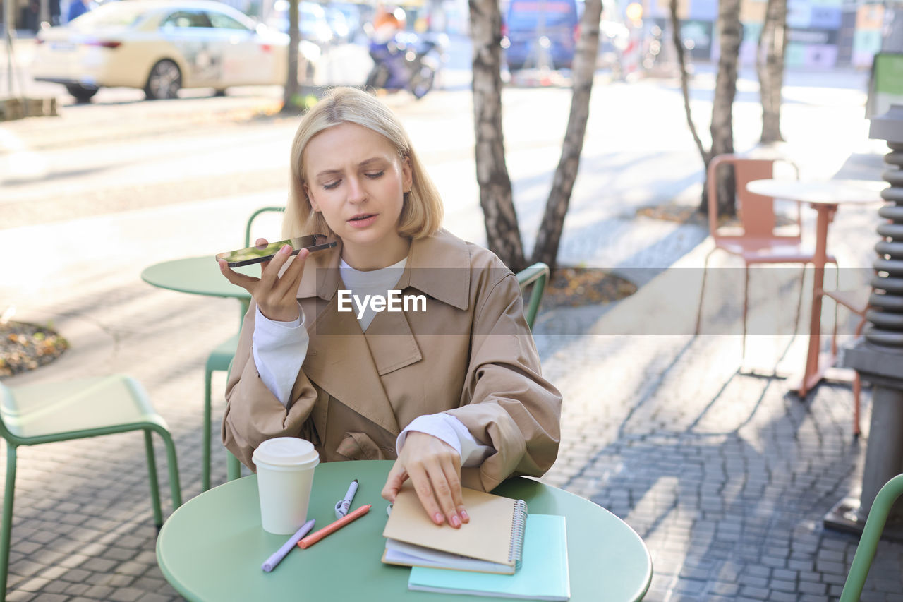 portrait of young woman using mobile phone while sitting at cafe