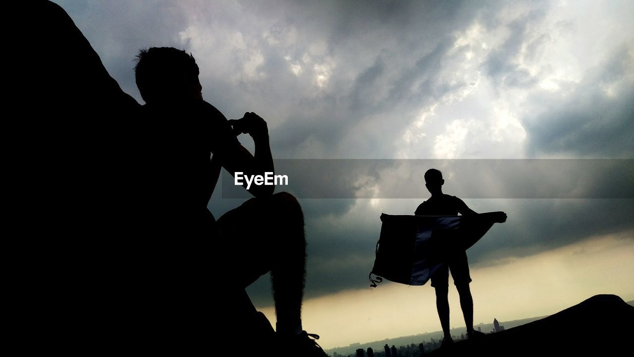 Silhouette of people on hill against cloudy sky