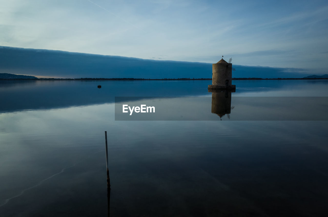 Traditional windmill in lake against sky during sunset