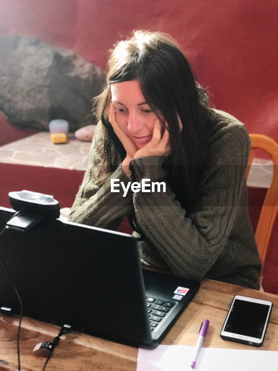 YOUNG WOMAN USING PHONE WHILE SITTING AT TABLE
