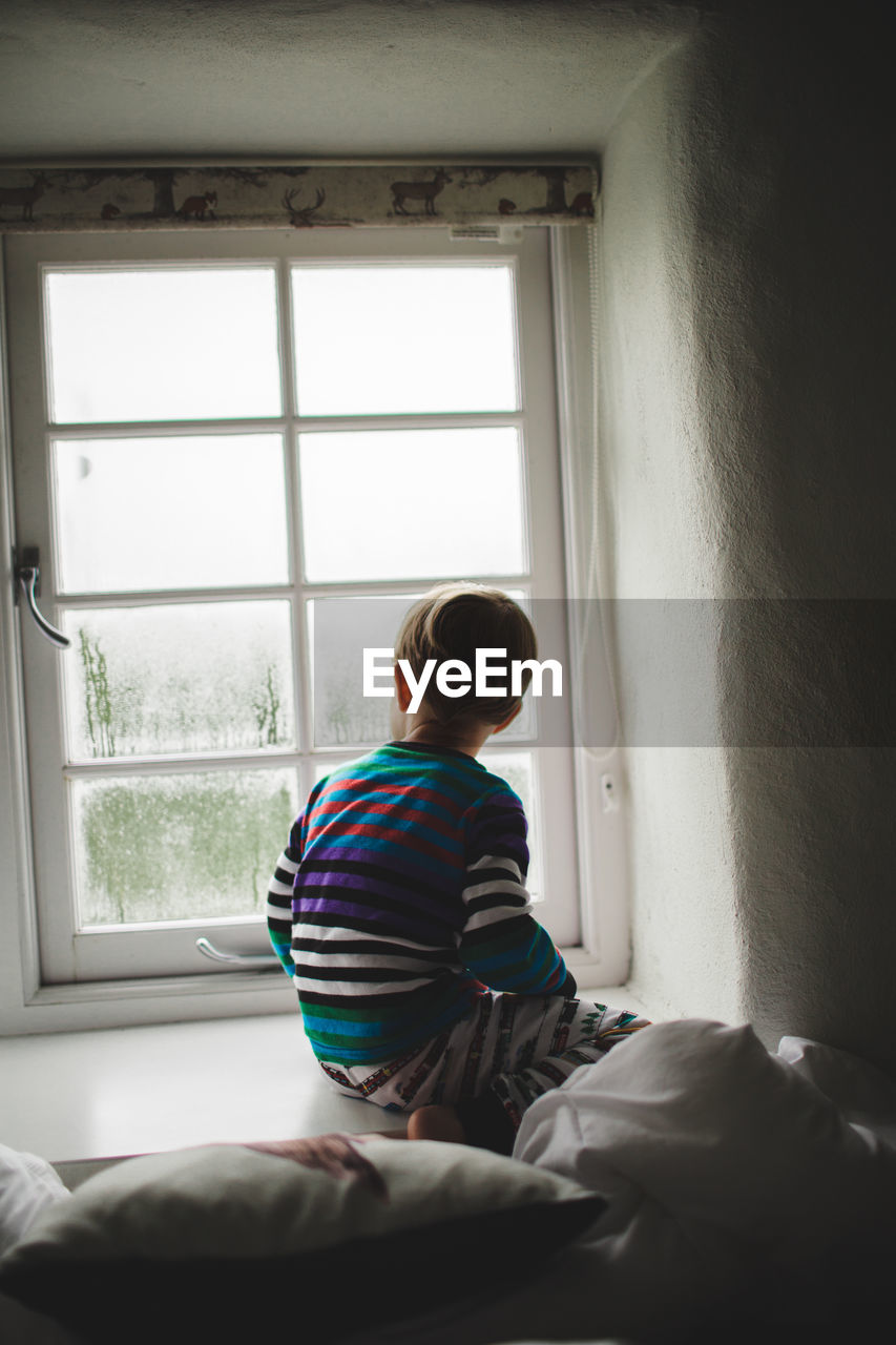 Rear view of boy looking through window at home