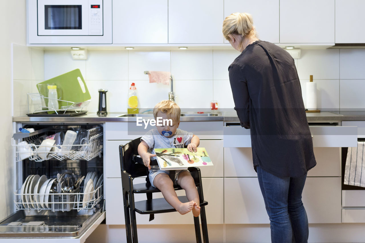 Mother working in kitchen while baby boy sitting on high chair