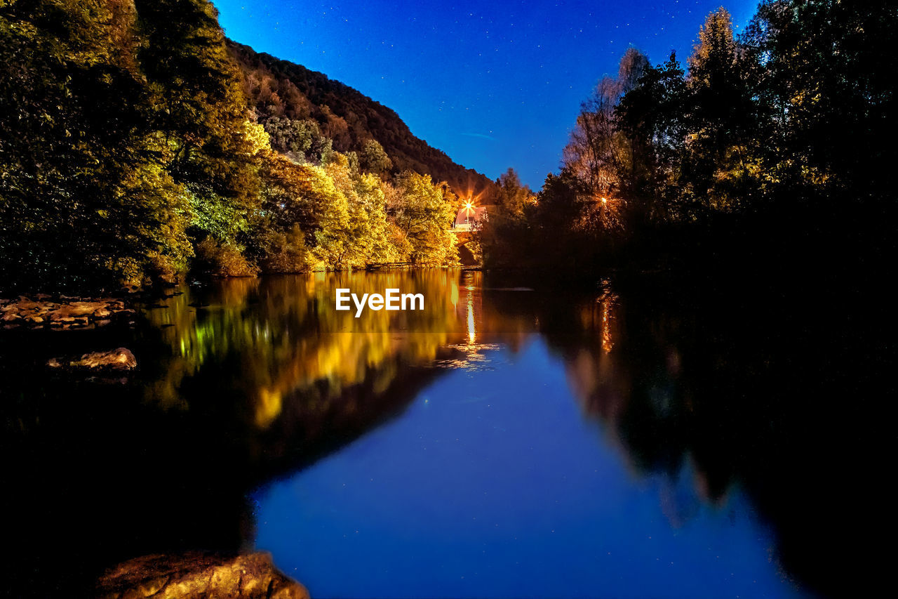 SCENIC VIEW OF LAKE AGAINST TREES AT NIGHT