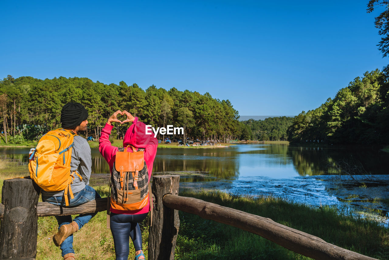 REAR VIEW OF PEOPLE BY LAKE AGAINST BLUE SKY