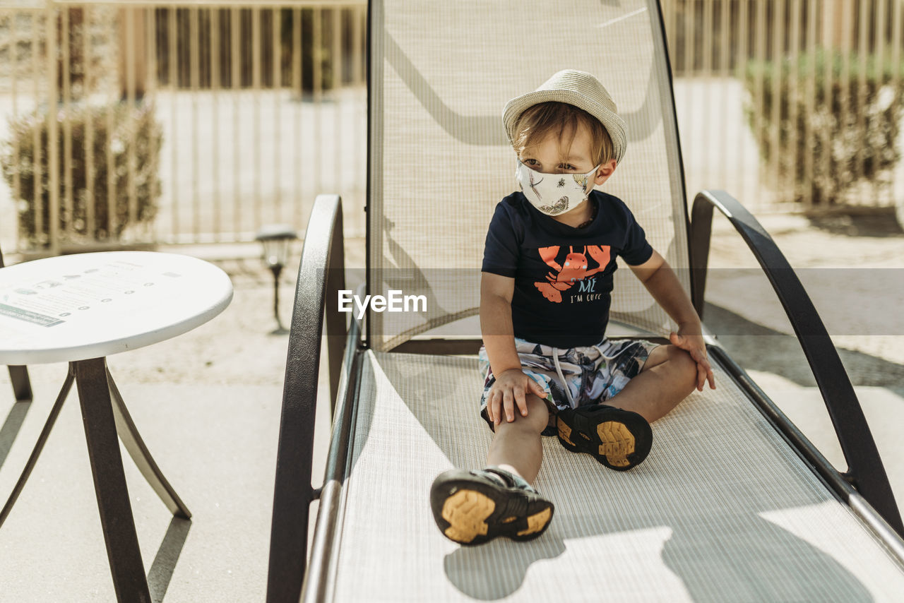 Young toddler boy with mask on sitting by pool in palm springs