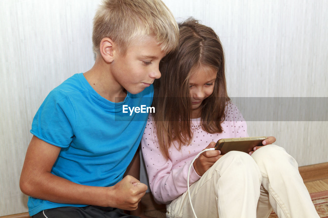 Cute boy and girl using smart phone sitting at home