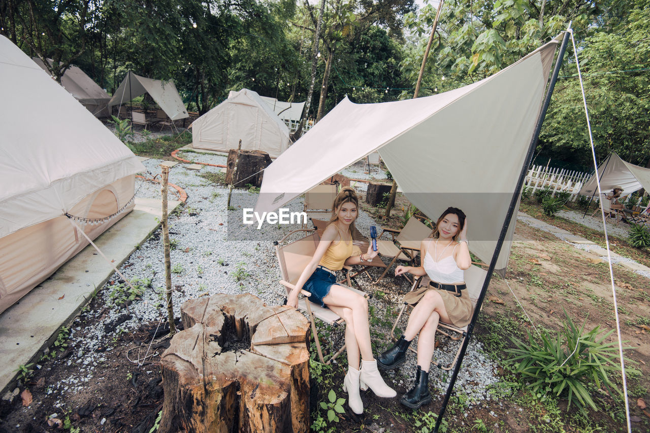 tent, adult, leisure activity, togetherness, women, camping, friendship, nature, lifestyles, full length, young adult, plant, happiness, men, group of people, enjoyment, tree, day, vacation, relaxation, trip, summer, sitting, holiday, female, smiling, emotion, bonding, outdoors, fun, casual clothing, carefree, weekend activities, travel, person, high angle view, clothing, cheerful, food and drink