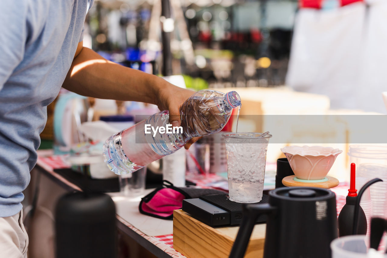 Barista hand pouring water into plastic glass with iced.