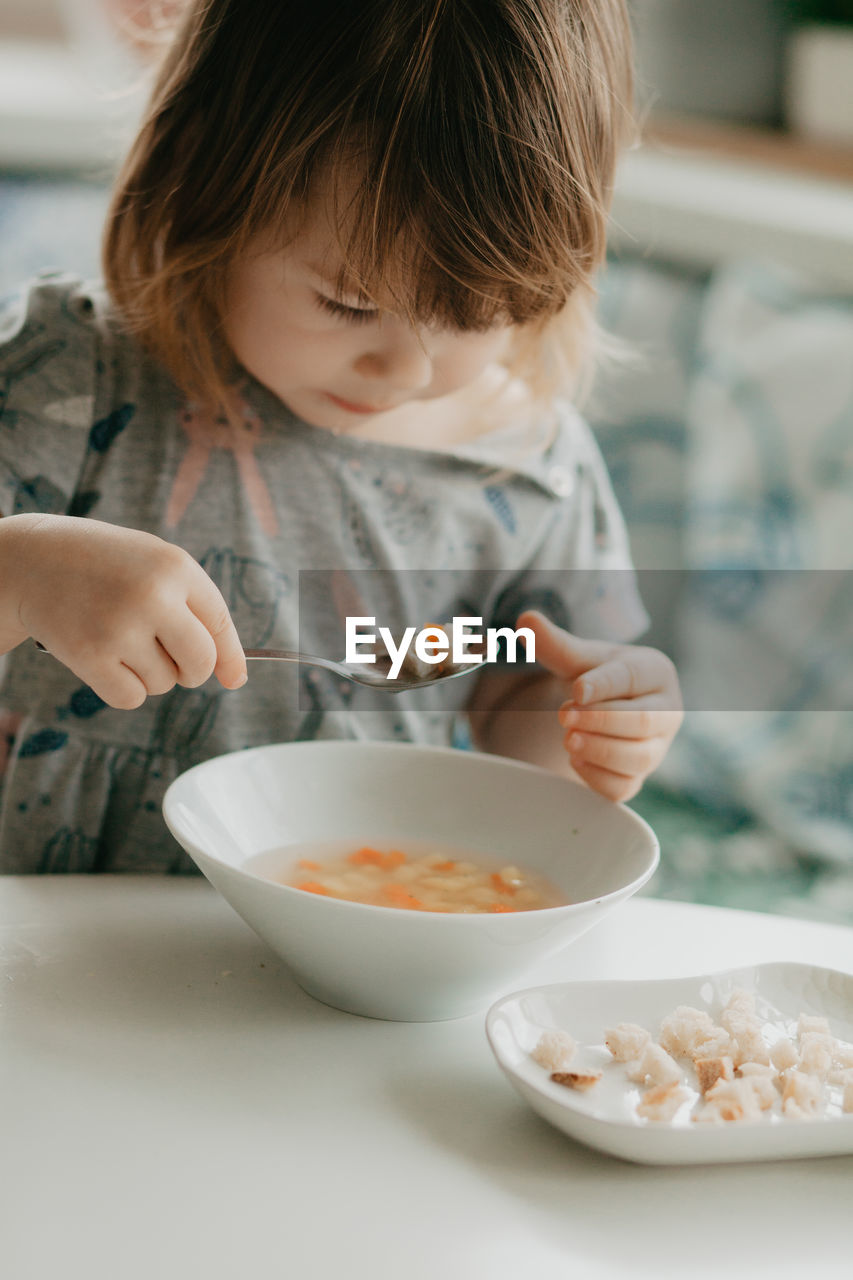 A little girl is sitting at the kitchen table eating soup. high quality photo