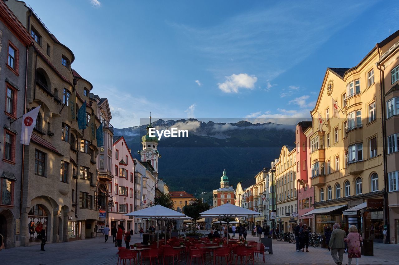 People on street amidst buildings in city with mountains in background 