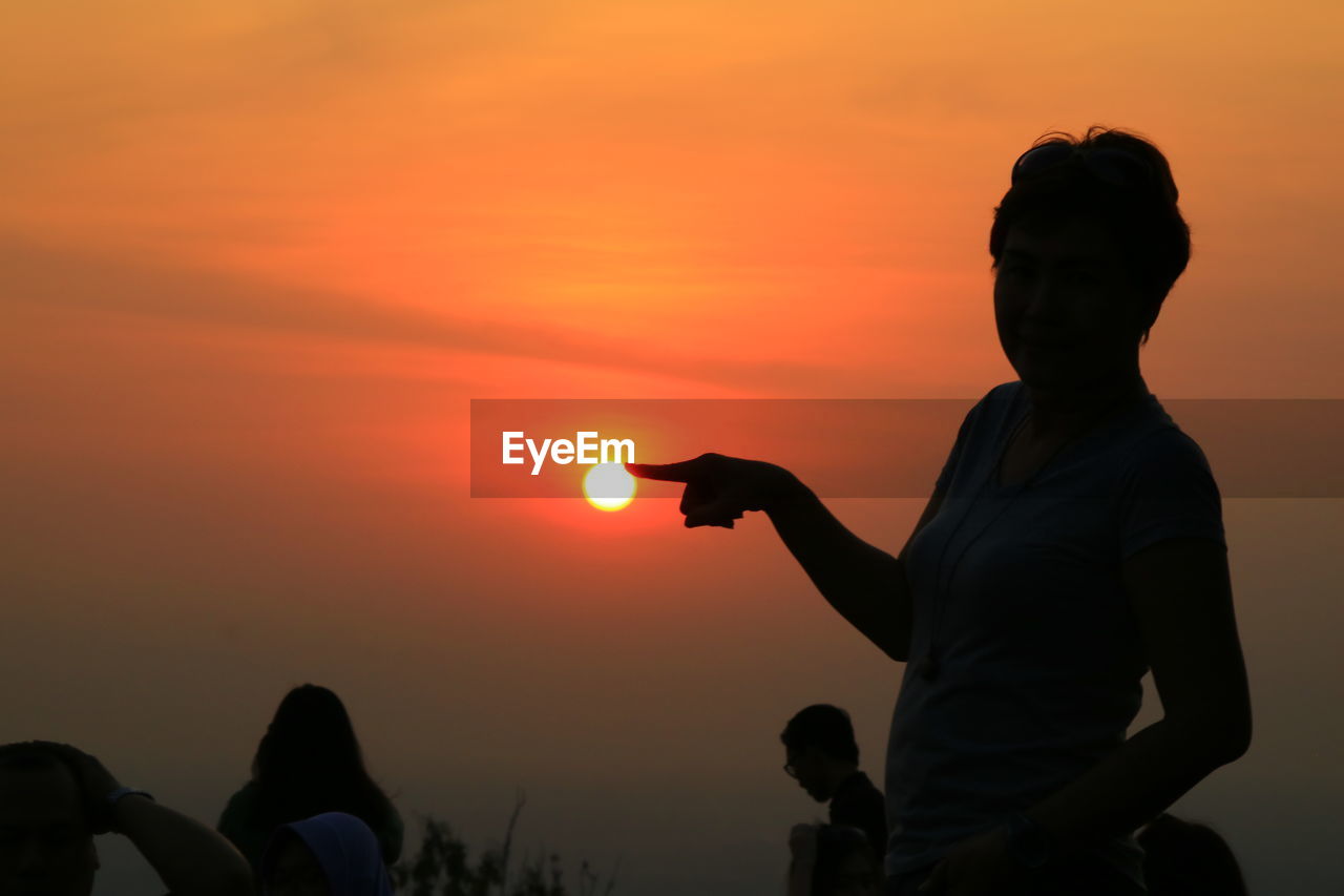 Silhouette woman standing against orange sky at sunset